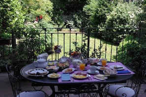 A round table with a variety of breakfast items, including eggs, toast, and fruit, set outdoors with a garden view.