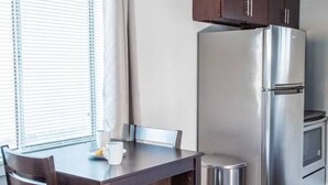 A compact kitchen with a stainless steel refrigerator, wooden cabinets, and a dining table with chairs.