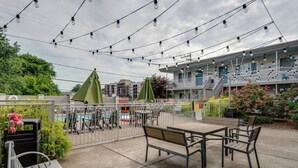 An outdoor patio area with tables and chairs, string lights overhead, and a view of a building with balconies.
