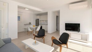 A modern living room with a flat-screen TV, a dining area with a white table and chairs, and a kitchen in the background. - Villa Athena - Villa near the Sea with pool on Corfu Island, Greece (Peritheia)