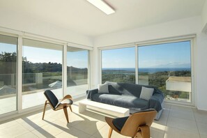 Een ruim balkon met een moderne bank en stoelen, grote glazen deuren en een prachtig uitzicht op het landschap.