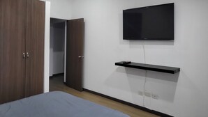 Une chambre à coucher comprenant un lit, une armoire, un téléviseur fixé au mur et une étagère située sous le téléviseur.