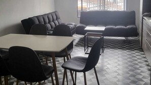 Un espace de vie moderne et compact, comprenant un canapé, une table à manger et des chaises. Une grande fenêtre offre une vue sur le paysage urbain.