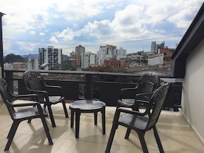 Un balcón con cuatro sillas negras y una mesa redonda pequeña, con vistas a un paisaje urbano con diversos edificios.
