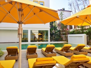 A poolside area with lounge chairs and umbrellas. - Bloomrooms @ Calangute (Calangute)