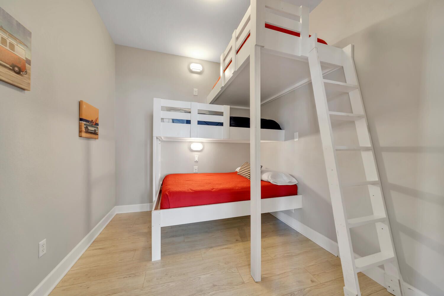 Dormitorio con literas, una escalera, un colchón rojo y un estante pequeño.