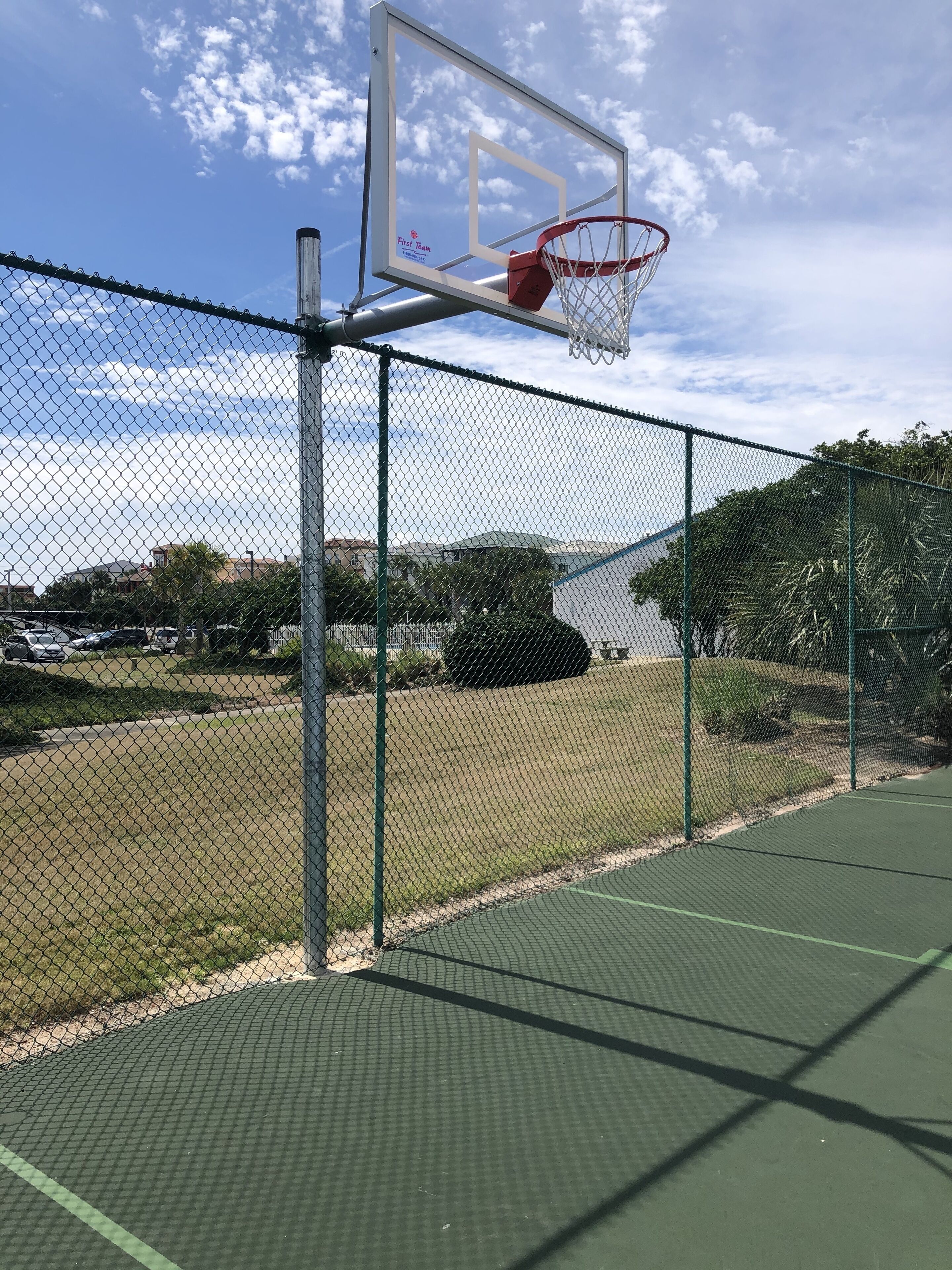 A basketball court with a chain-link fence, a basketball hoop, and a clear sky.