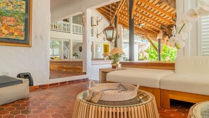 Una habitación acogedora con techo de madera, un sofá, una cesta de mimbre y vistas a un balcón con plantas.