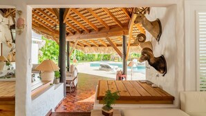 Un espacio interior acogedor con techo de madera, una cabeza de venado montada y vista a una piscina al aire libre.