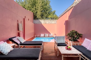 A poolside area with lounge chairs and a table, surrounded by pink walls and a wooden deck.