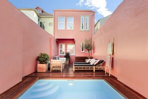 A modern pool area with wooden decking, a lounge chair, and a small table. - Casa da Praça (Porto)
