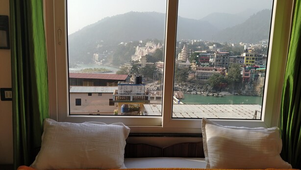 Habitación de hotel con cama, cortinas verdes y ventana que ofrece vistas a un paisaje urbano y montañas.