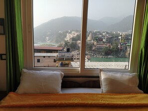 A hotel room with a bed, green curtains, and a window offering a view of a cityscape and mountains.