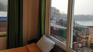 Una habitación de hotel con un ventanal grande, una cama con una colcha naranja y vistas a un río y edificios.