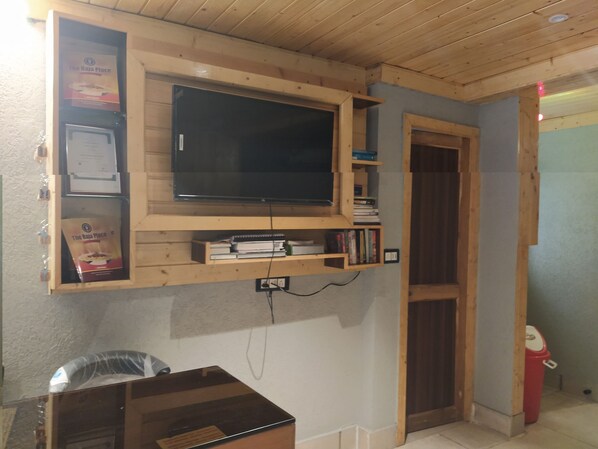 A room with a wooden TV shelf, a trash bin, and a door.