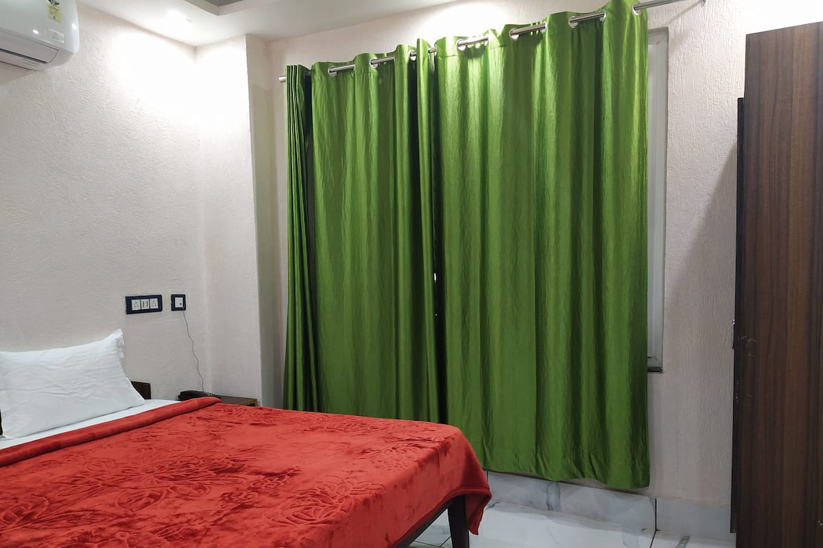 A hotel room with a bed, green curtains, a white wall, and a wooden door.