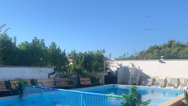A swimming pool with a clear blue water, surrounded by a poolside area with lounge chairs and potted plants. - Maison Rinaldi (Bari)