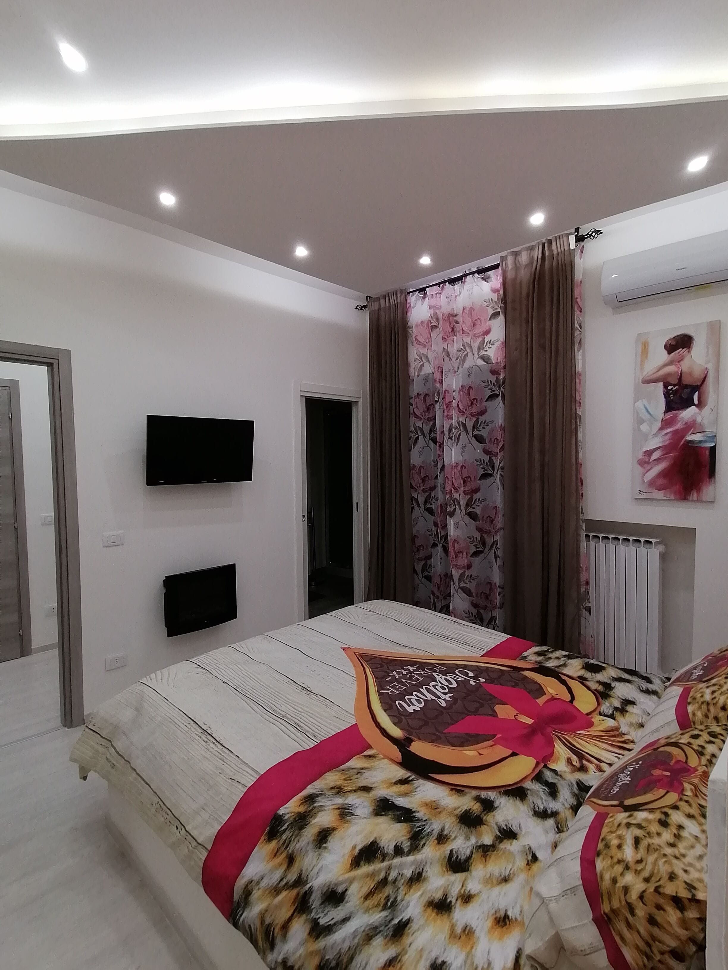 A bedroom with a bed, a flat-screen TV, a radiator, and a painting on the wall.