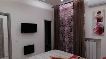 A bedroom with a bed, a flat-screen TV, a radiator, and a painting on the wall.