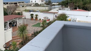 A residential area with a view of the sea, a white building with a red roof, and a paved courtyard with potted plants. - Maison Rinaldi (Bari)