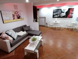 Un salon moderne avec un canapé d’angle gris, une table basse blanche agrémentée d’un arrangement floral, et un mur d’accent rouge.