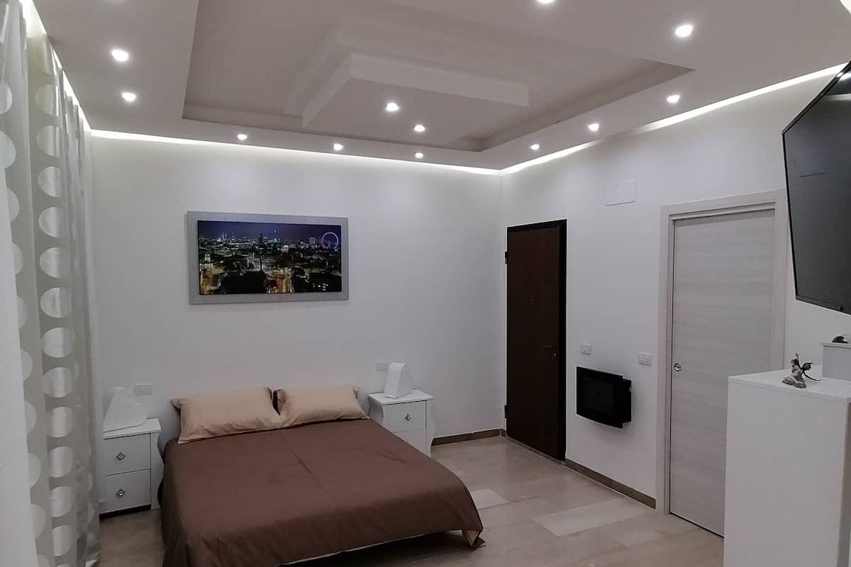 Quarto moderno com cama, mesas de cabeceira, televisão de tela plana e uma porta.