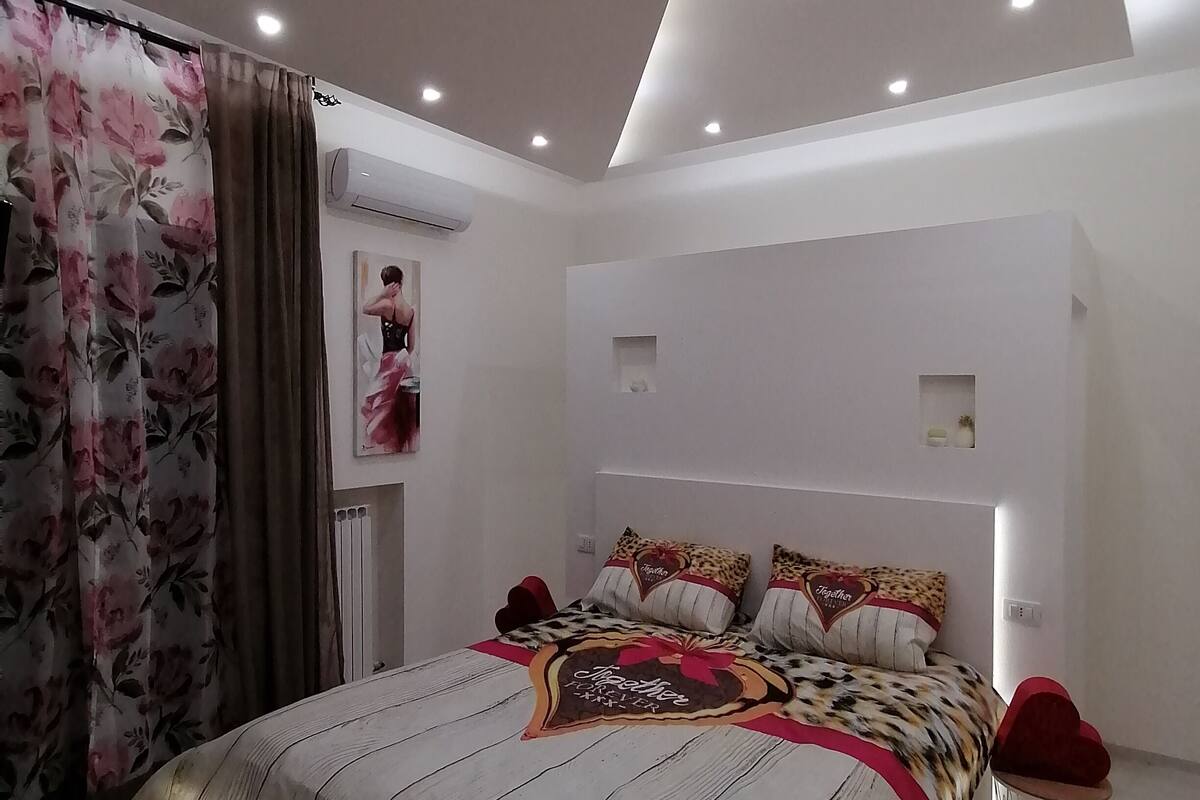 Quarto moderno com cama, cortinas e luminária no teto.