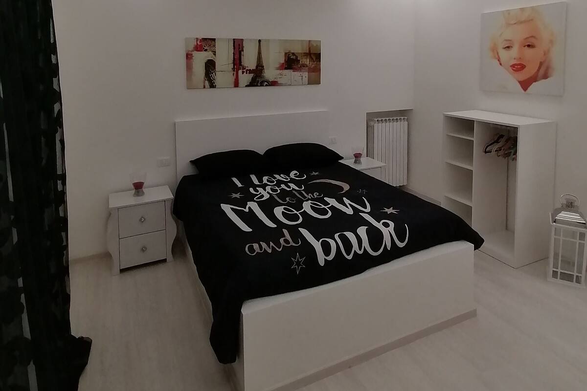 Quarto moderno com cama, mesa de cabeceira, cômoda e radiador.
