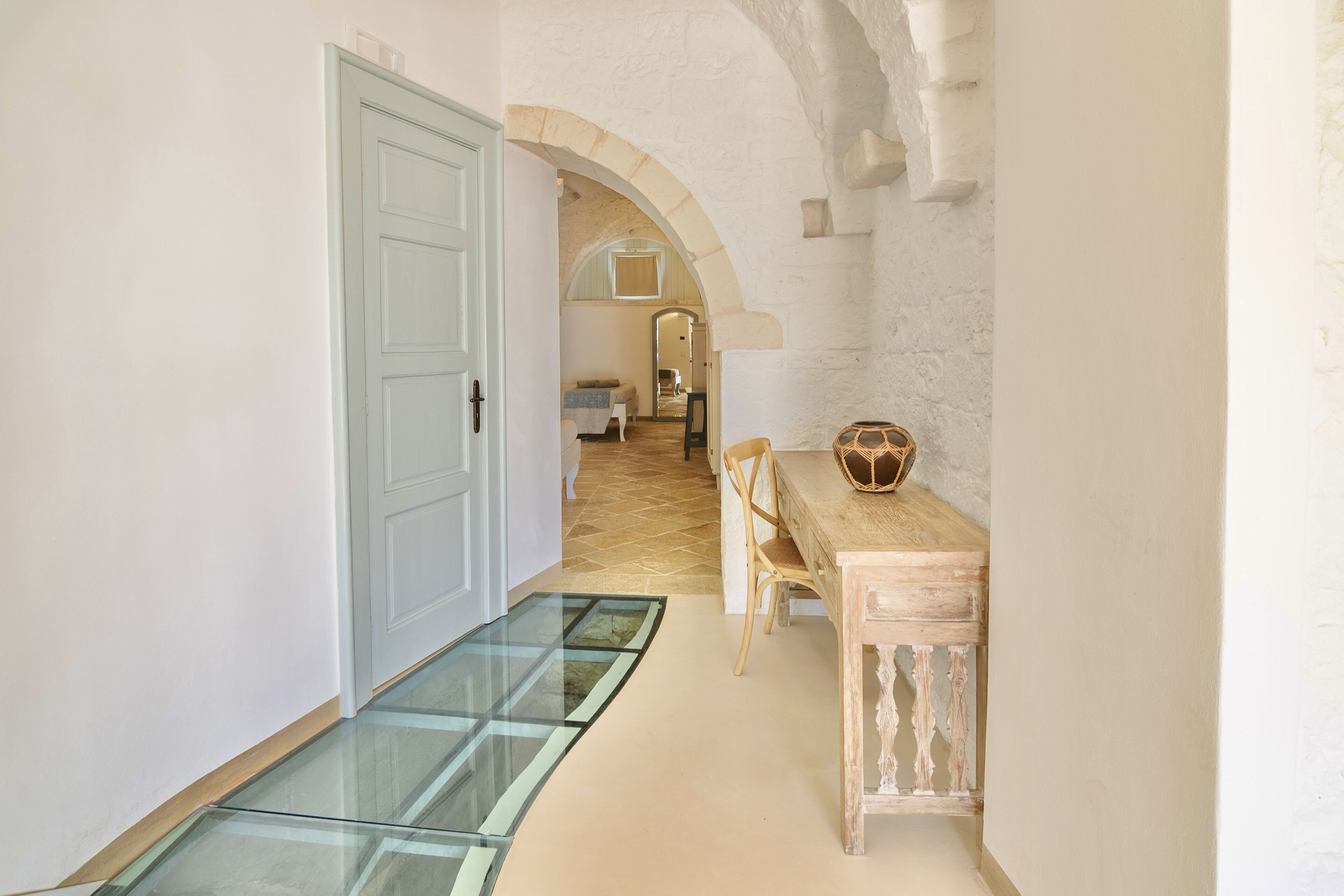 A hallway with a glass door, a dining area with a table and chairs, and an arched stone wall.