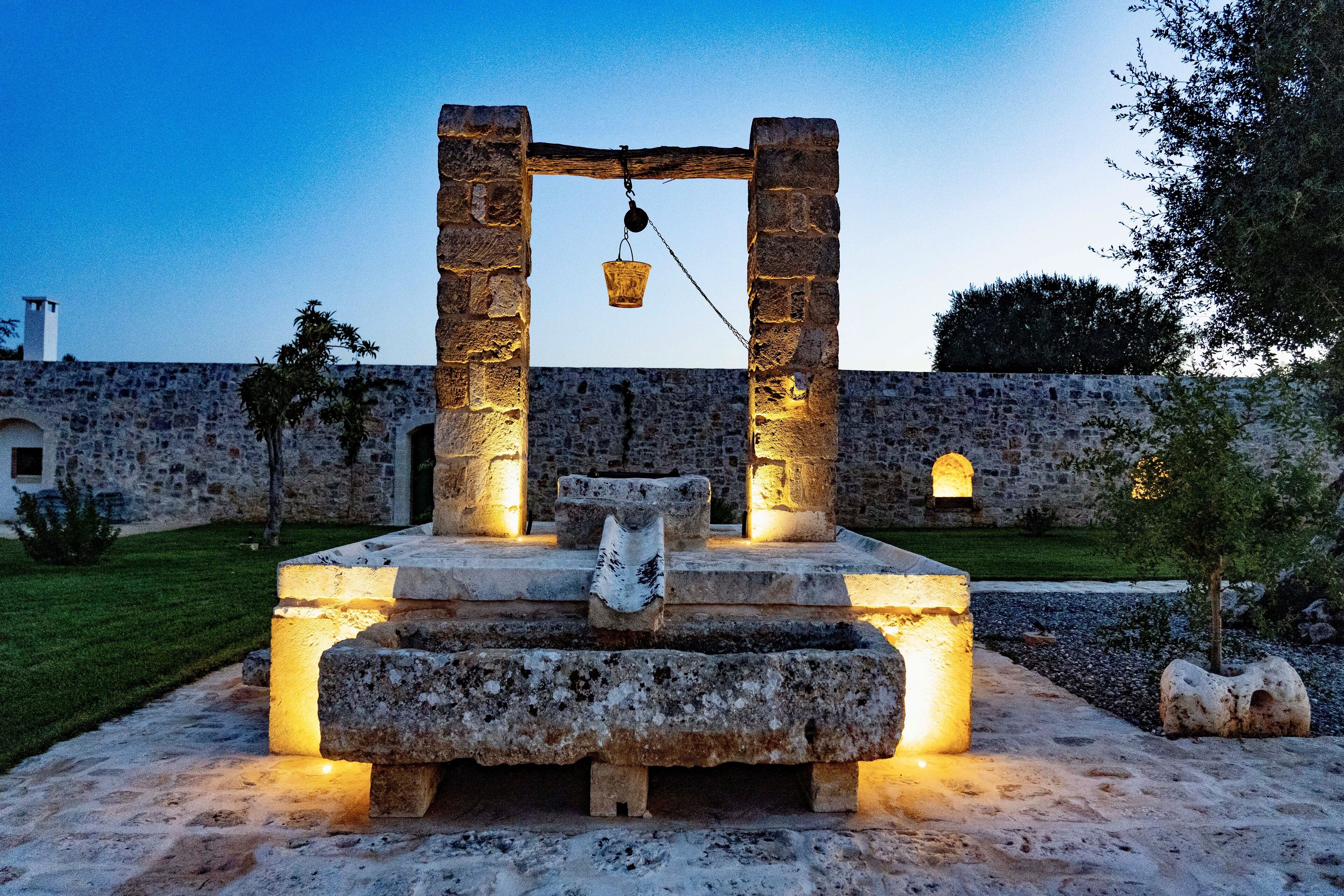 Una construcción de piedra con una cesta colgante, rodeada por un muro de piedra y una zona cubierta de césped.