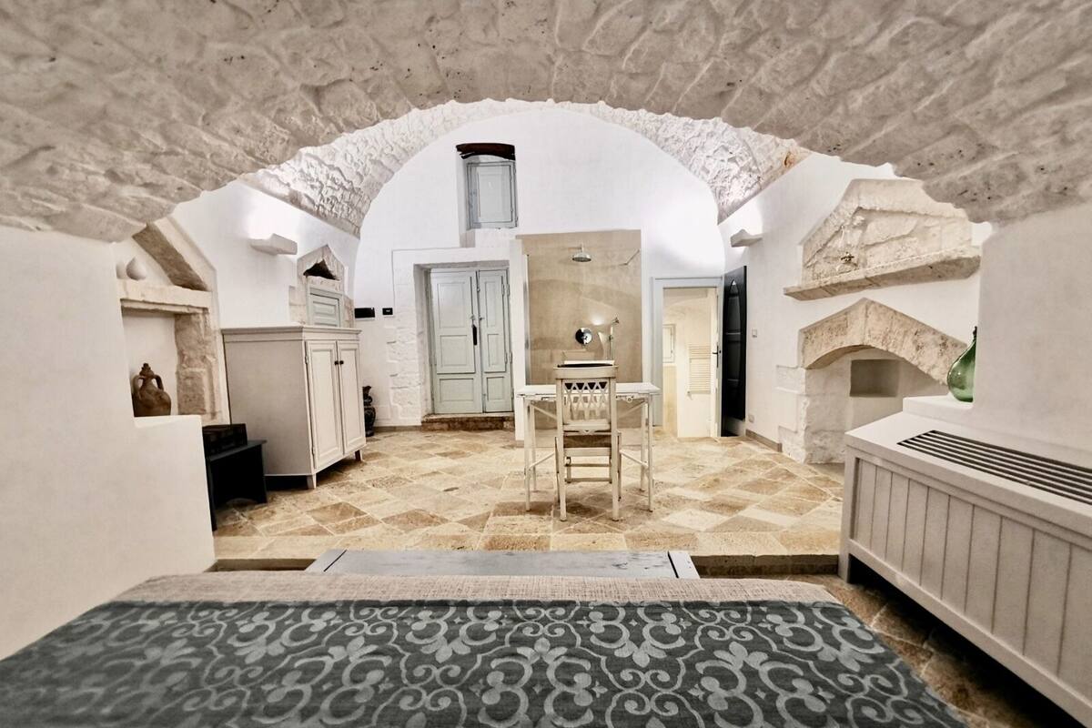 A cozy, stone-walled room with a rustic aesthetic, featuring a small table and chair, a door, and a fireplace.