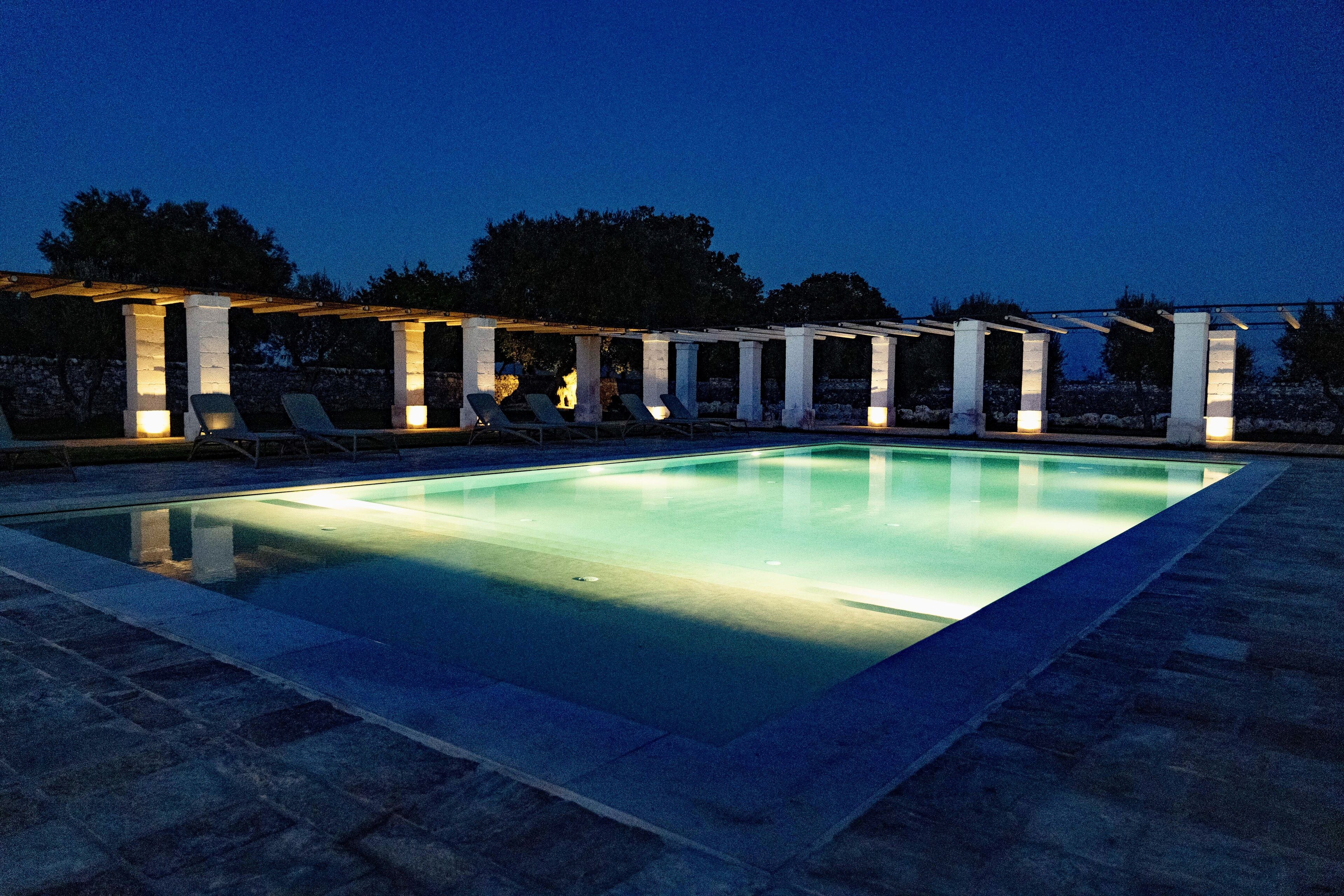 A rectangular swimming pool with a pergola and lounge chairs.