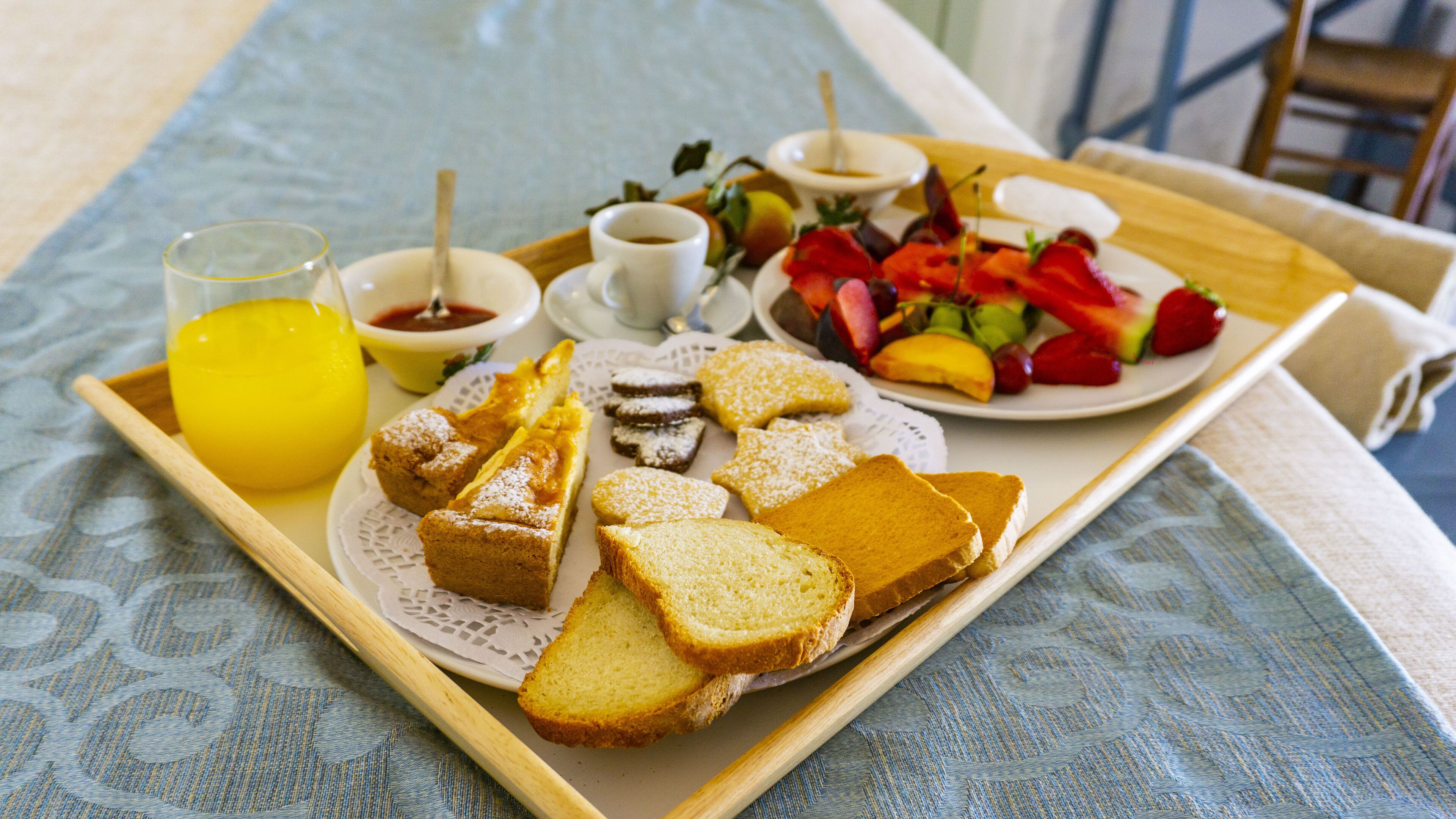 Un plateau contenant divers éléments pour le petit-déjeuner, notamment des toasts, des viennoiseries, des fruits et un verre de jus d’orange.