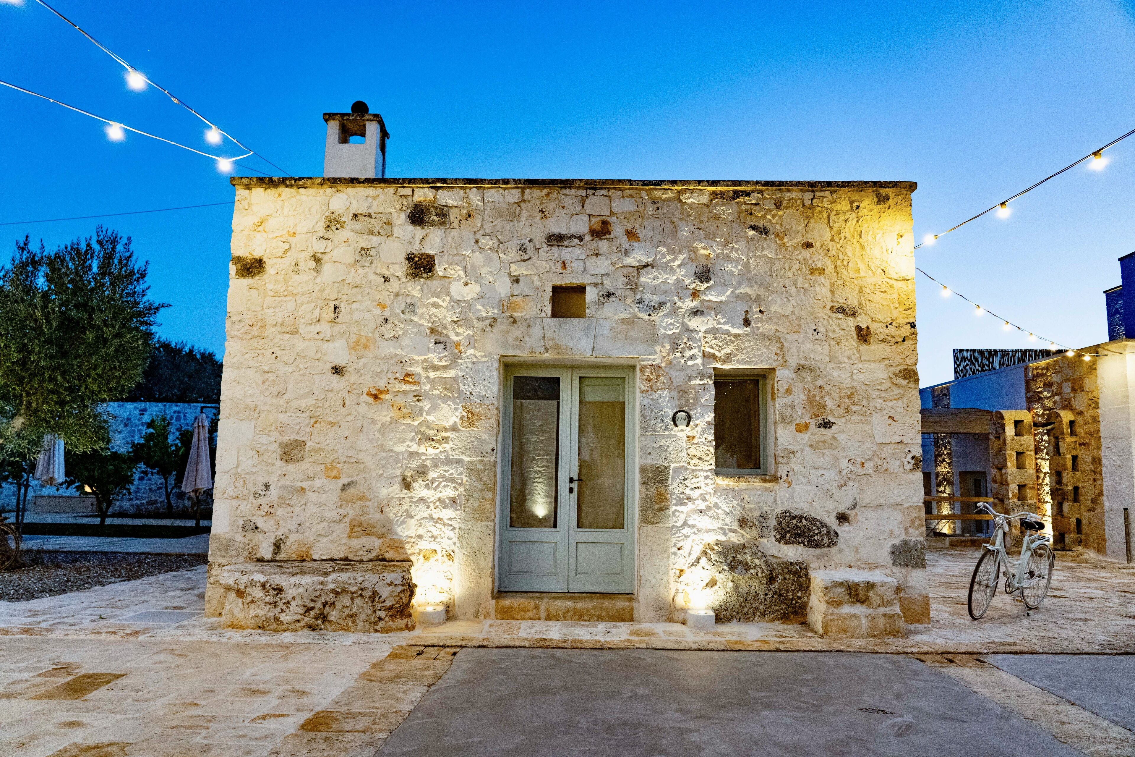 A stone building with a door, a bicycle, and string lights.