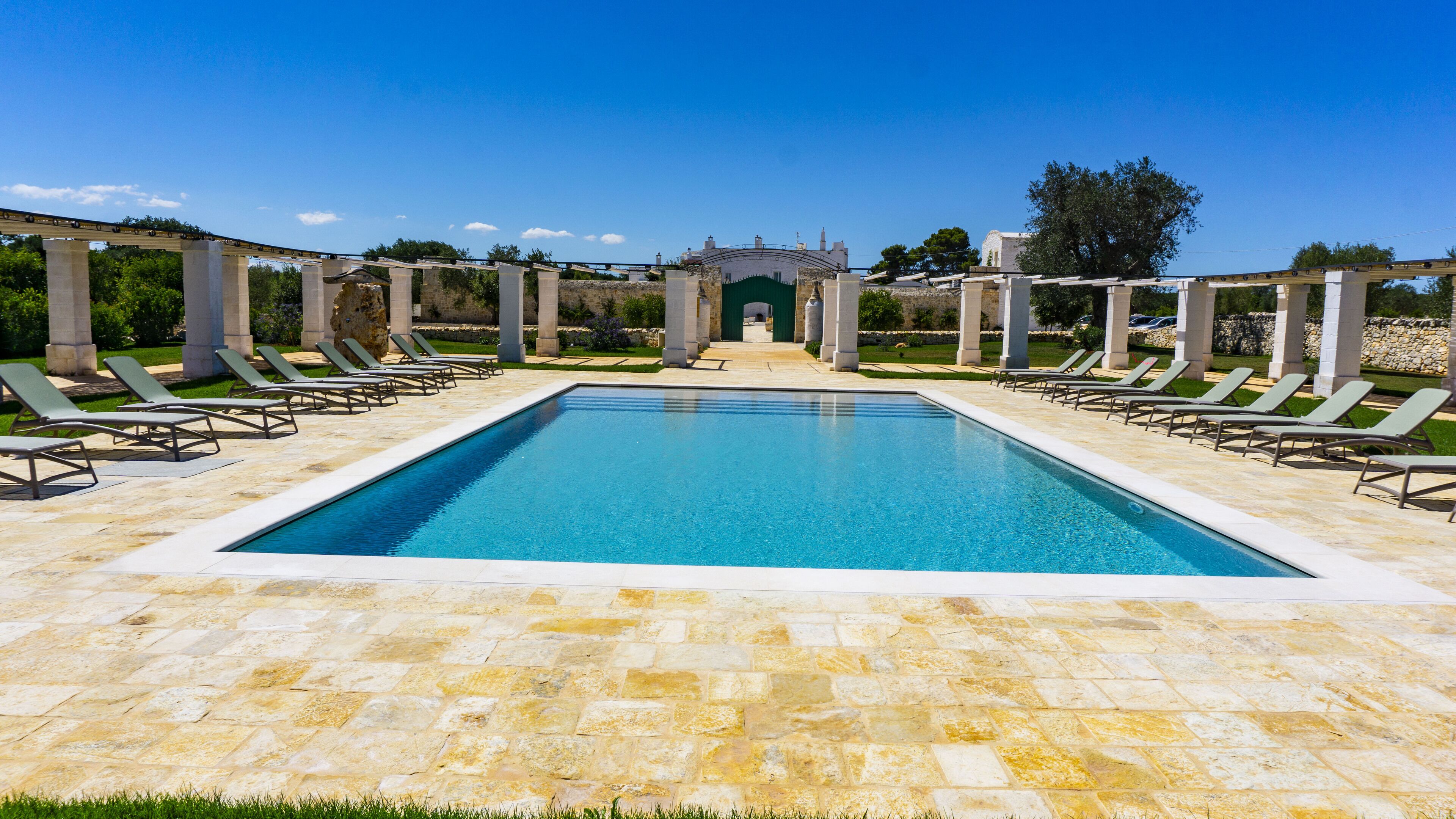 Ein rechteckiger Pool mit einer Steindeck, umgeben von Liegestühlen und einer Steinmauer.