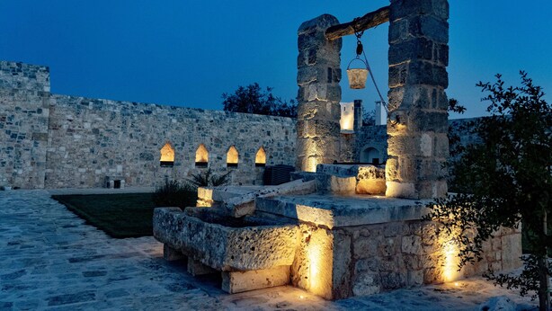 Estructura de piedra con ventanas iluminadas y un muro de piedra al fondo.