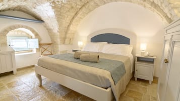 A bedroom with a stone vaulted ceiling, a bed with a blue headboard, and a window with a view.