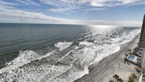 A beach view with a building adjacent to the shore, featuring a swimming pool and a deck area. - 1206 Waters Edge Resort 1 Bedroom Condo by RedAwning (Murrells Inlet)