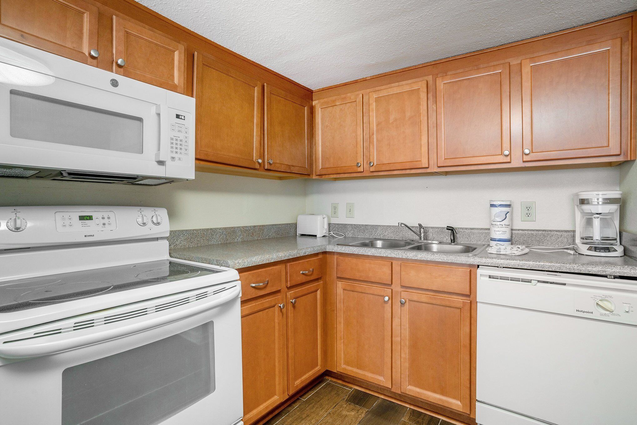 A kitchen with wooden cabinets, a microwave, a stove, a sink, a coffee maker, and a dishwasher.