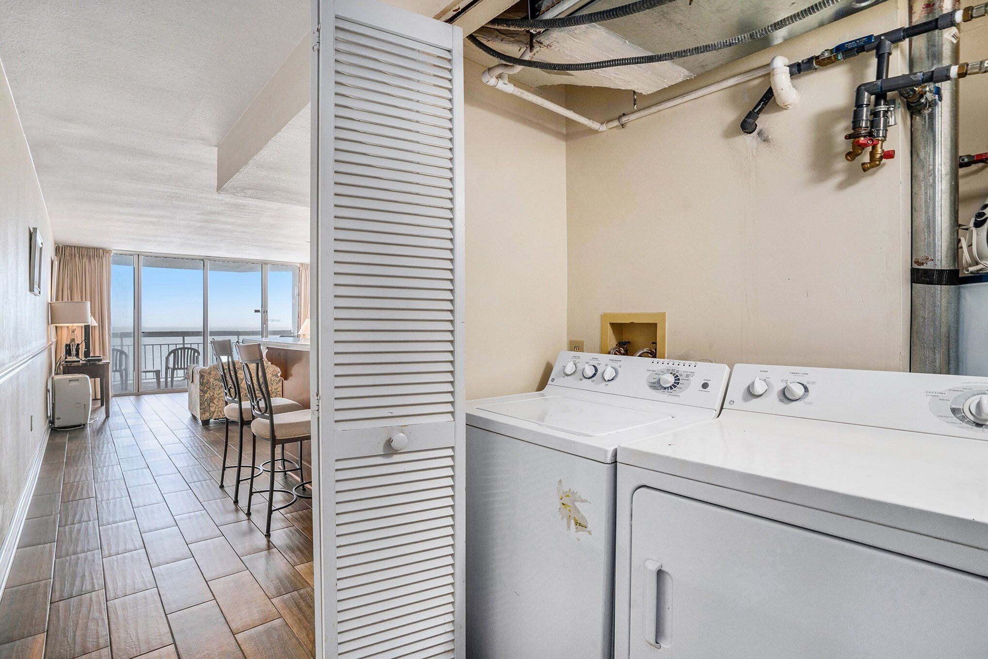 A laundry area with a washing machine and dryer, a dining area with chairs and a table, and a view through a large window.