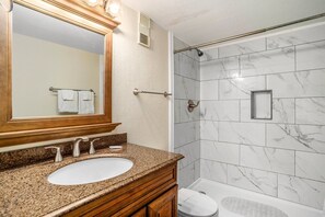 A bathroom with a granite countertop sink, a large mirror, and a shower with marble tiles. - 0610 Waters Edge Resort 1 Bedroom Condo by RedAwning (Murrells Inlet)