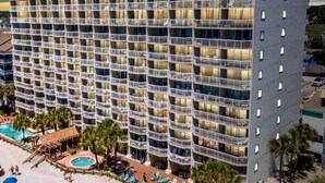 Un hôtel à plusieurs étages doté de balcons, d’un espace piscine et de chaises longues.