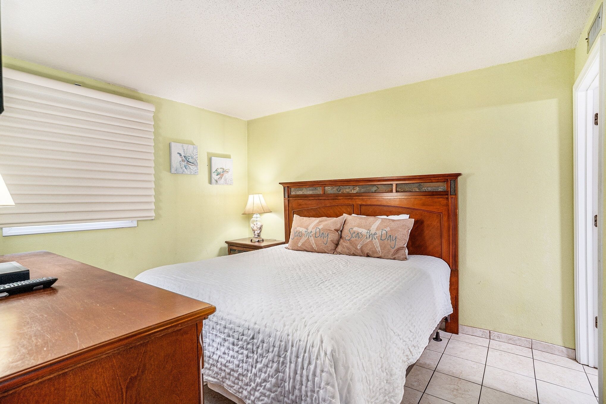 A bedroom with a bed, bedside table, lamp, and a window with blinds.