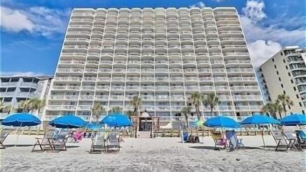 A large hotel with a uniform exterior, multiple balconies, and a beach area with umbrellas and lounge chairs. - 0407 Waters Edge Resort 1 Bedroom Condo by RedAwning (Murrells Inlet)