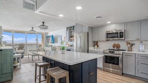 A modern kitchen with a large island, stainless steel appliances, and a view of the beach. - 0407 Waters Edge Resort 1 Bedroom Condo by RedAwning (Murrells Inlet)