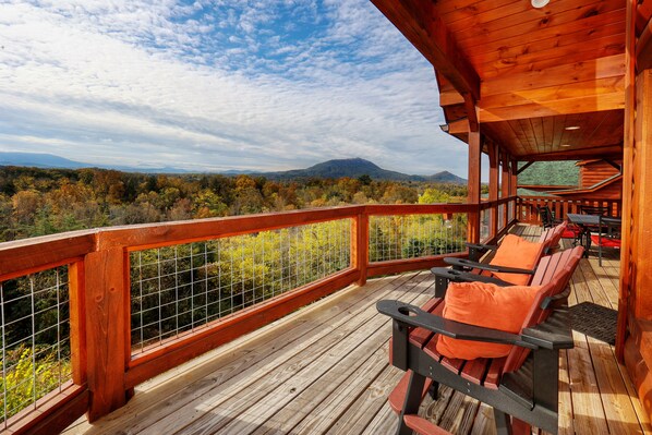 Una terraza de madera con mobiliario exterior y vistas a un paisaje montañoso.