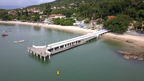 A pier extending into calm waters with boats and a beach in the background. - Pousada Praia do Trapiche (Penha)