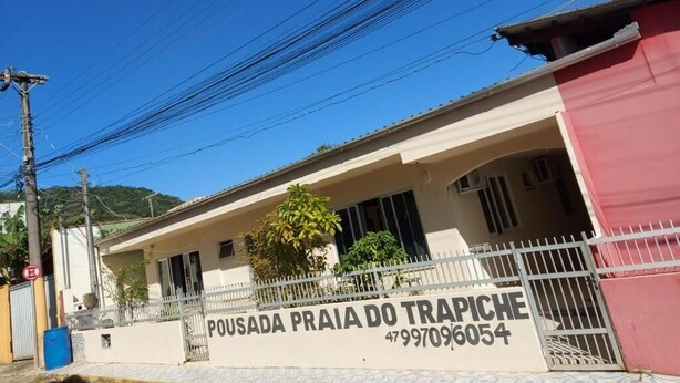 A building with a sign reading "POUSADA PRAIA DO TRAPICHE" and a contact number. - Pousada Praia do Trapiche (Penha)
