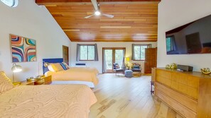 A bedroom with two beds, a ceiling fan, a TV, and a large window.