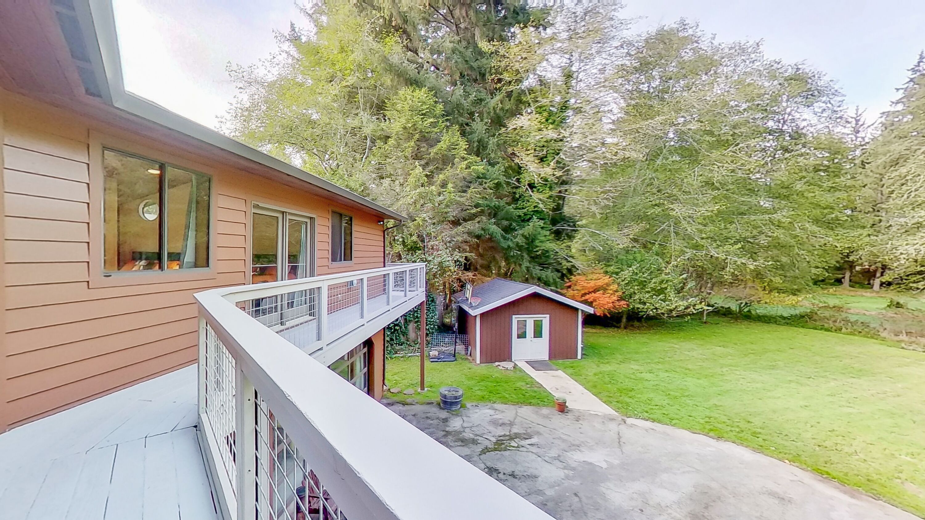 Une maison à deux étages avec un balcon, un petit abri de jardin et une pelouse bien entretenue.